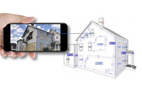 Person holding up phone with image of a house. In background, a drawing of that same house.