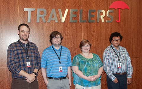 Four people standing under a Travelers sign.